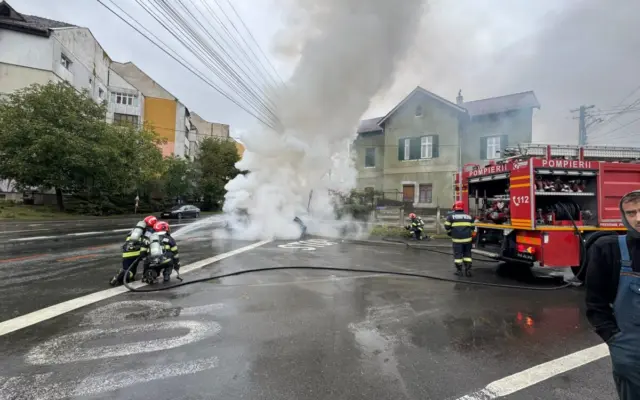 Pompieri români care intervin la locul unui accident rutier unde o mașină a luat foc sau scoate fum dens