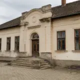 O fațadă veche de clădire cu un singur etaj, având un portal de intrare monumental cu scară și ușă masivă din lemn