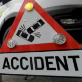 Un panou de avertizare rutieră de formă triunghiulară, cu margini roșii, plasat în fața unui vehicul de intervenție