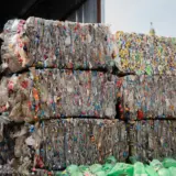 O stivă de baloturi compacte de deșeuri reciclabile, în special sticle de plastic și ambalaje de diverse culori, depozitate într-o hală de sortare