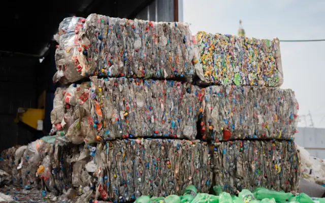 O stivă de baloturi compacte de deșeuri reciclabile, în special sticle de plastic și ambalaje de diverse culori, depozitate într-o hală de sortare
