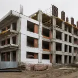 O clădire cu mai multe etaje aflată în stadiul de șantier, cu structura de beton și zidăria de cărămidă parțial vizibile