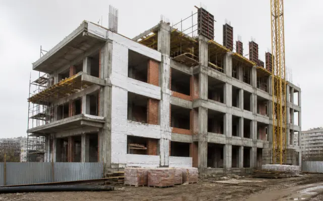 O clădire cu mai multe etaje aflată în stadiul de șantier, cu structura de beton și zidăria de cărămidă parțial vizibile