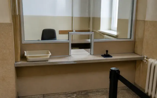 Un ghișeu interior dintr-o instituție publică, prevăzut cu un geam de protecție și un mic orificiu pentru schimbul de documente
