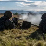 Two soldiers in camouflage uniforms operating a machine gun during military training in a grassy field
