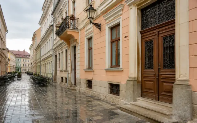 O stradă pietonală istorică, pavată cu piatră cubică umedă, mărginită de clădiri vechi cu arhitectură clasică în nuanțe de pastel