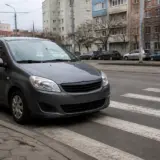 Un autoturism de culoare gri închis este oprit la marginea unei treceri de pietoni marcate cu dungi albe pe asfalt